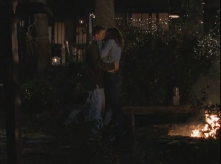 Long shot of Pacey and Joey kissing by campfire, arms around each other.