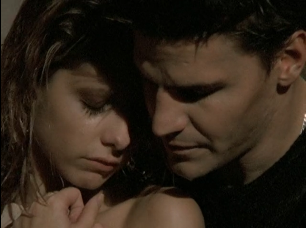 Buffy and Angel, with Buffy's shoulders bare, nuzzle their foreheads against each other, looking sad.